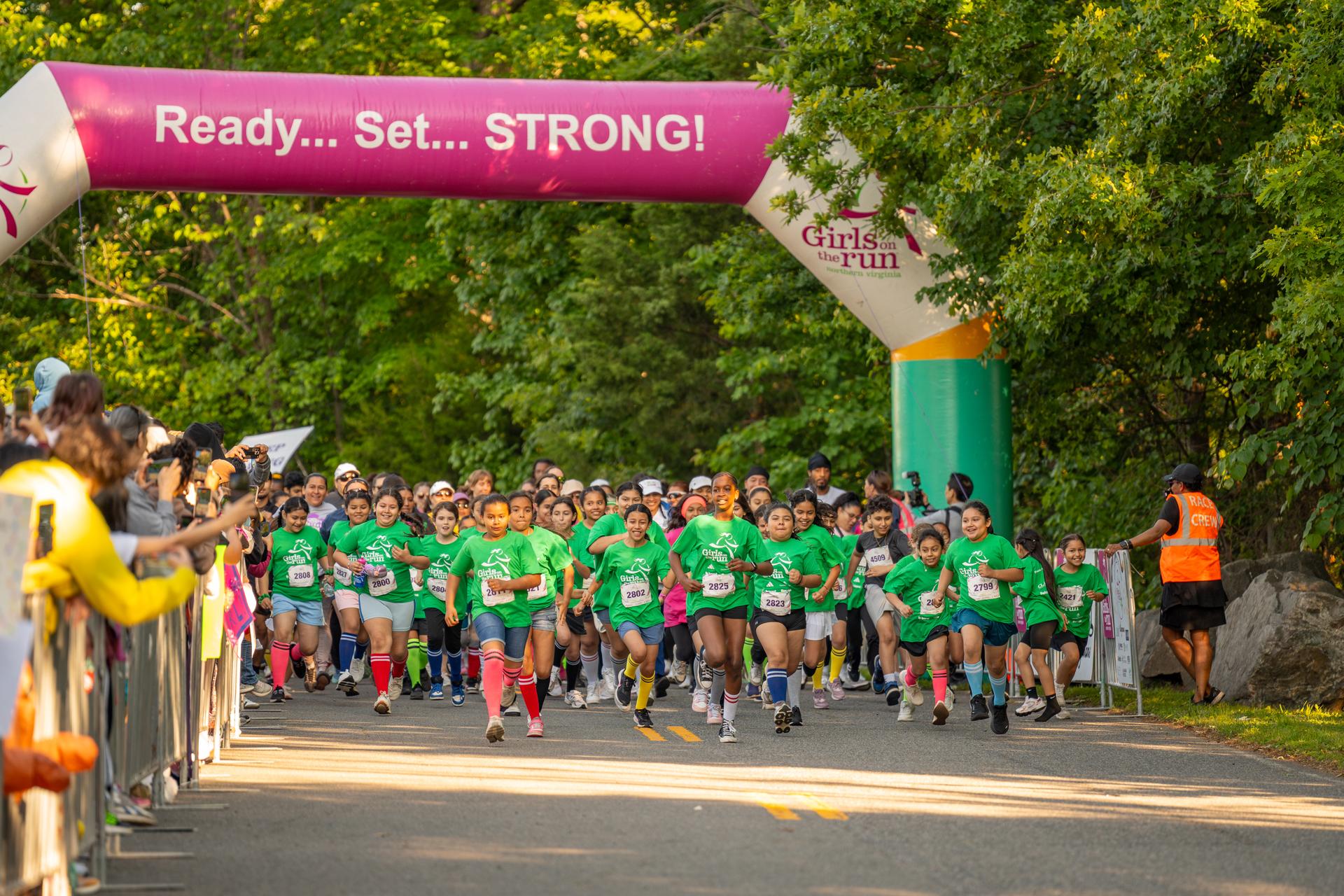 Hundreds of Girls on the Run participants starting the 5K by running under an inflatable arch that reads 