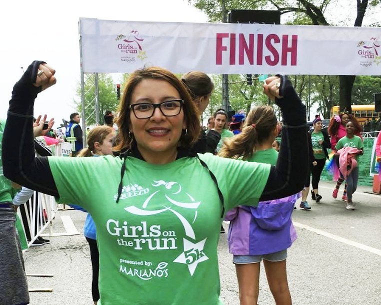 Coach Yessenia Jacome smiling and flexing her muscles after crossing the finish line at the GOTRC 5K