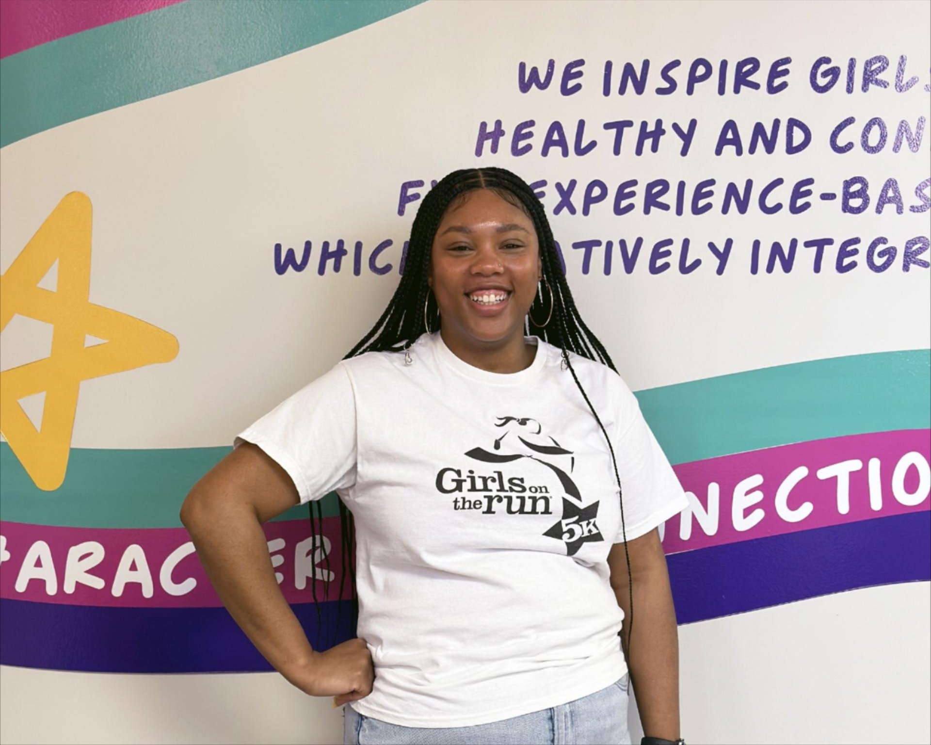 KaMia wearing a Girls on the Run 5K t-shirt, smiling in front of the vinyl artwork at GOTRC's office